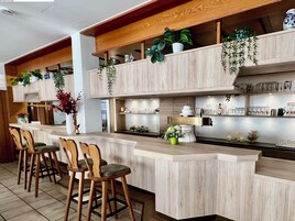 Eine Bar mit Holzsesseln, Regalen mit Pflanzen und diversen Barutensilien.