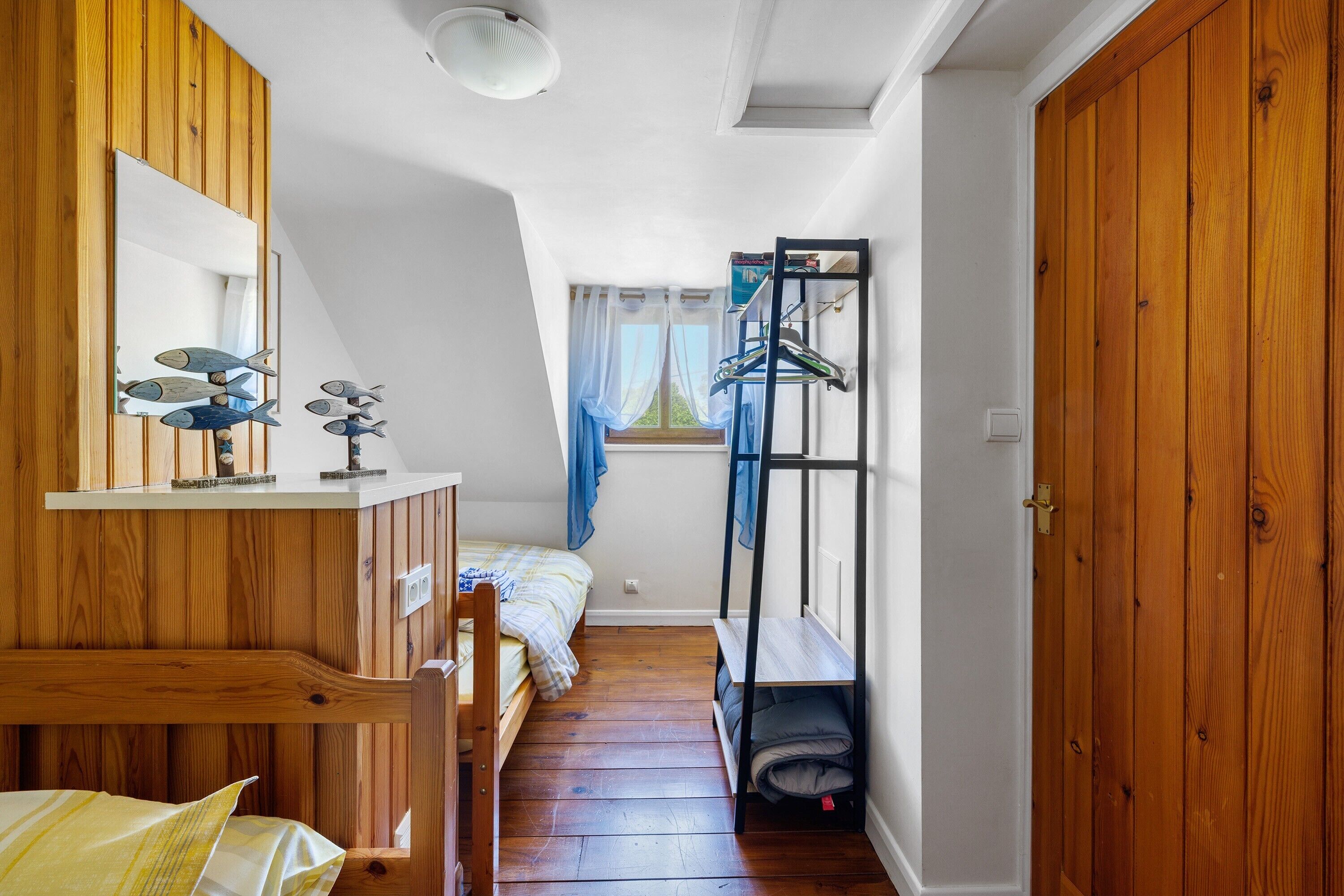 A bedroom with a bunk bed, wooden walls, a mirror, and a window with curtains.