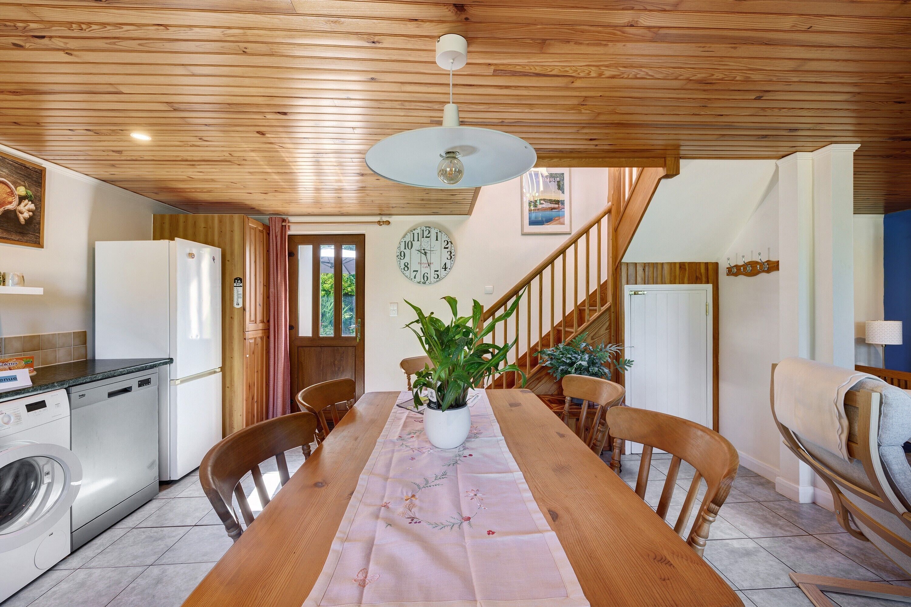 Un comedor con una mesa de madera, sillas, un reloj y una escalera.