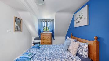 Una camera da letto con un letto, una cassettiera, una sedia e una finestra con tende.