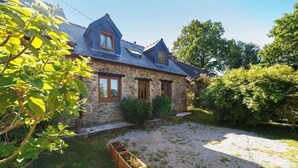 A stone house with a sloped roof, wooden window frames, and a gravel driveway. - Apartment “La Poya” with Private Terrace, Garden, and Wi-Fi (Plonévez-du-Faou)