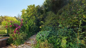 A garden with a brick pathway, various plants, and a wooden planter. - Apartment “La Poya” with Private Terrace, Garden, and Wi-Fi (Plonévez-du-Faou)