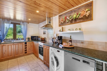 A kitchen with wooden cabinets, a washing machine, a coffee maker, and a window with curtains.. Apartment “La Poya” with Private Terrace, Garden, and Wi-Fi