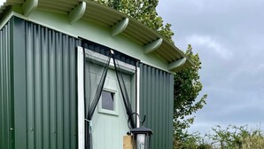 Un cobertizo verde pequeño con una puerta, un banco y un farol.