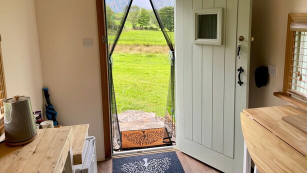 Una habitación con puerta de madera, una ventana pequeña, un timbre y vistas a un área verde exterior.