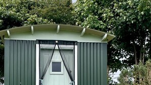 Un cobertizo pequeño verde con una puerta, un banco y un farol.