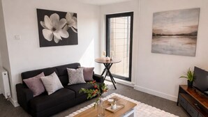 A modern living room with a black sofa, a white coffee table, and a large window. - Luxury 2BR Apartment - Free parking (Slough)