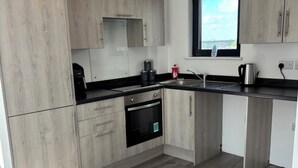 A modern kitchen with light wood cabinets, a black countertop, a built-in oven, and a window with a view. - Luxury 2BR Apartment - Free parking (Slough)