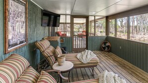 A covered porch with striped furniture, a television, and a framed poster on the wall.