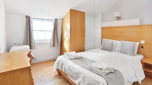 Een moderne hotelkamer met een houten bed, witte beddengoed, een bureau en een raam met gordijnen.