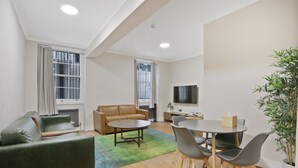 Een moderne woonkamer met een bank, een salontafel, een eettafel met stoelen, een televisie en een kamerplant.
