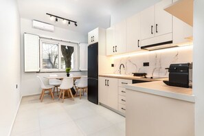 A modern kitchen with white cabinets, a black refrigerator, a coffee machine, and a dining area with a table and chairs. - MT Central Stay Old town (Kos)