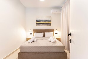 A neatly made bed with white linens and two rolled towels, a wooden headboard, a wall-mounted air conditioner, and a framed picture above the bed. - MT Central Stay Old town (Kos)