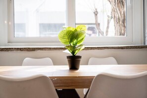 A conference table with a potted plant in the center, white chairs around, and a window with a view of trees and buildings. - MT Central Stay Old town (Kos)