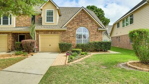 A two-story brick house with a front garage, a well-maintained lawn, and a clear sky.