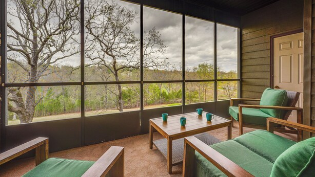 Quarto com uma janela grande, uma mesa de madeira, um sofá verde e uma cadeira.