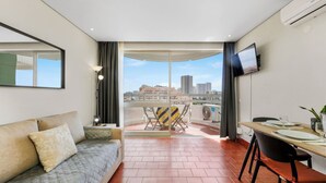 Quarto de hotel moderno com varanda, sofá, mesa de jantar e televisão.