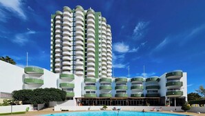 Um hotel com uma piscina grande, várias varandas e um edifício alto ao fundo.