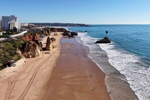 A coastal beach with rocky cliffs, a sandy shoreline, and buildings in the background. - Oasis 7 by Meditrust (Portimão)