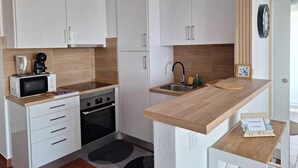 Uma cozinha compacta com armários brancos, micro-ondas, cafeteira, pia e um pequeno balcão com relógio e um objeto decorativo.