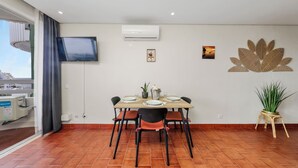 Uma sala de jantar com mesa posta para quatro pessoas, uma televisão de tela plana na parede e um vaso de planta.