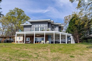 A modern two-story house with a covered patio, a staircase leading to the upper level, and a fenced backyard. - Greenwood Group Retreat w/ Large Private Dock! (Greenwood)