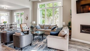 A spacious living room with a large window, a ceiling fan, and a fireplace. - Greenwood Group Retreat w/ Large Private Dock! (Greenwood)