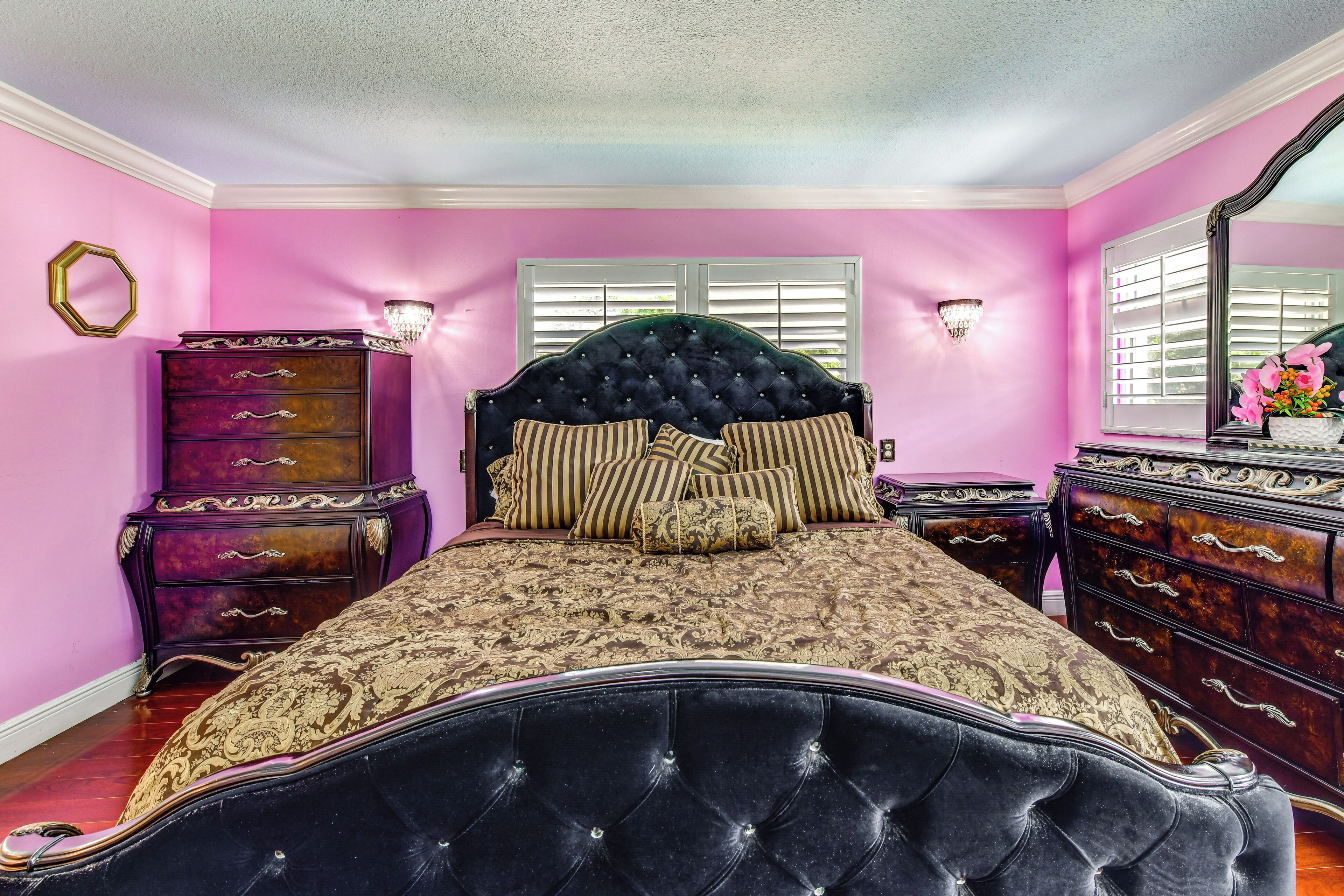 Une chambre à coucher avec une tête de lit capitonnée, un grand lit avec une literie à motifs, une commode avec des tiroirs et un miroir au mur.
