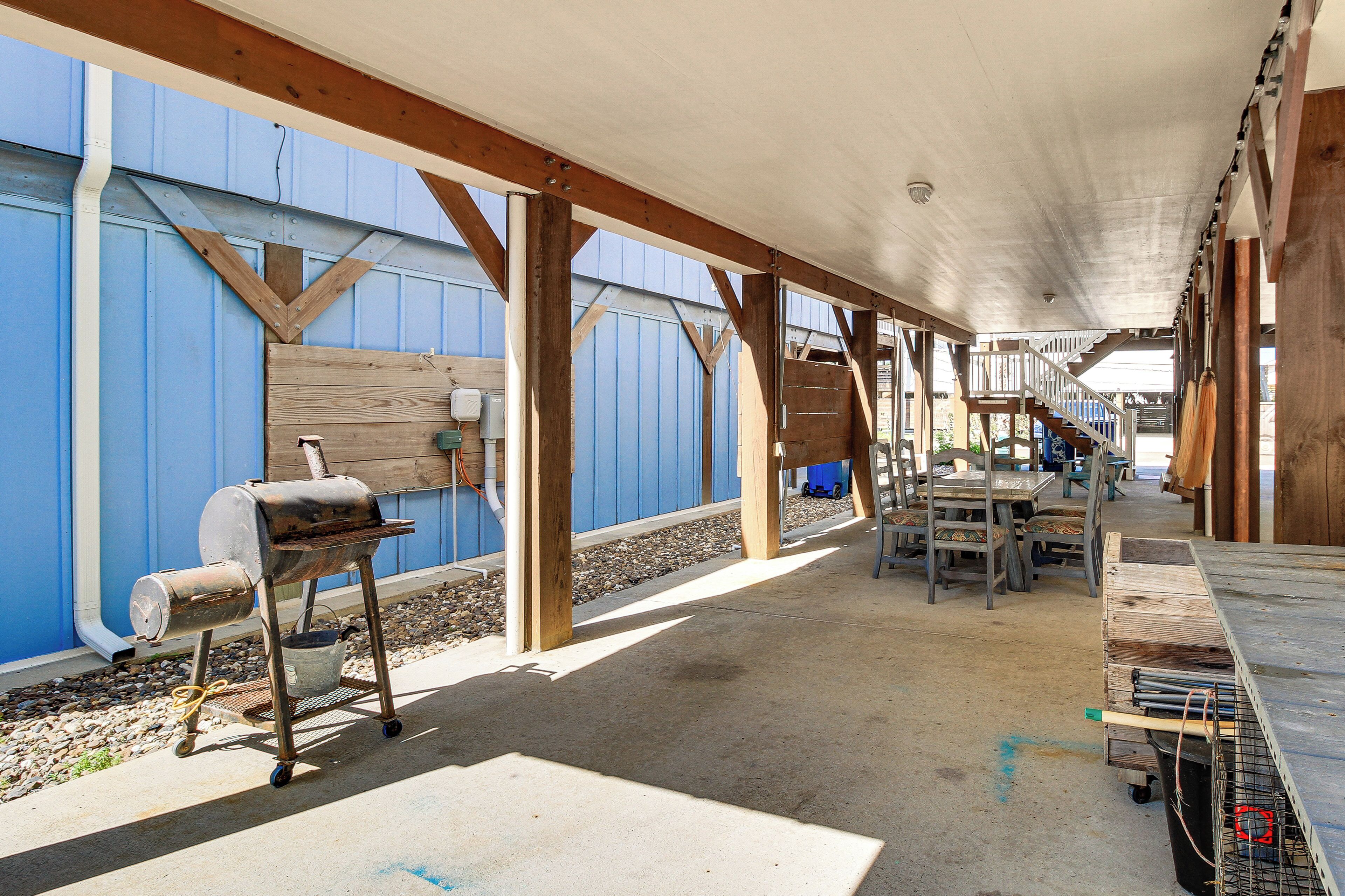 An outdoor covered patio area with a barbecue grill, tables, and chairs.