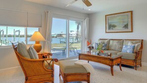 A living room with wicker furniture, a ceiling fan, and a large window with a view of the water. - Home w/ Views & Dock on Lemon Bay Aquatic Preserve (Englewood)