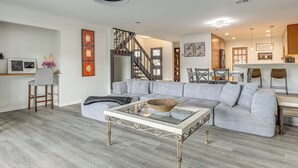 Een ruime woonkamer met een grote grijze modulaire bank, een glazen salontafel en een trap naar een hoger niveau.