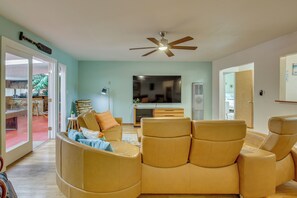 A living room with a sofa, a ceiling fan, a flat-screen TV, and a dining area visible through glass doors.