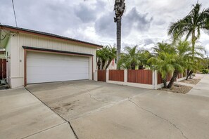A residential garage with a concrete driveway, a wooden fence, and palm trees.