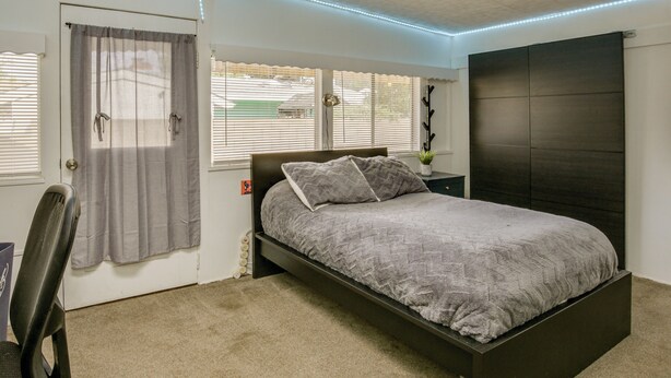Un dormitorio con cama, una silla, una ventana con persianas y una puerta.