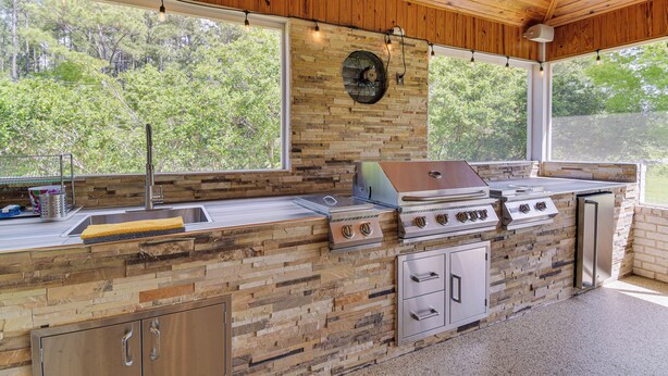 Una cocina al aire libre con protector de piedra, electrodomésticos de acero inoxidable y vistas del bosque circundante.