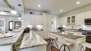 Una cocina moderna con armarios blancos, encimeras de granito y taburetes de bar.