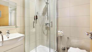 Ein modernes Badezimmer mit einer Duschkabine, einem weißen Waschbecken und einem Spiegel darüber.
