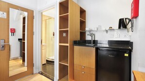 Eine kleine Küche mit einem schwarzen Kühlschrank, Holzschränken und einer Kaffeemaschine.