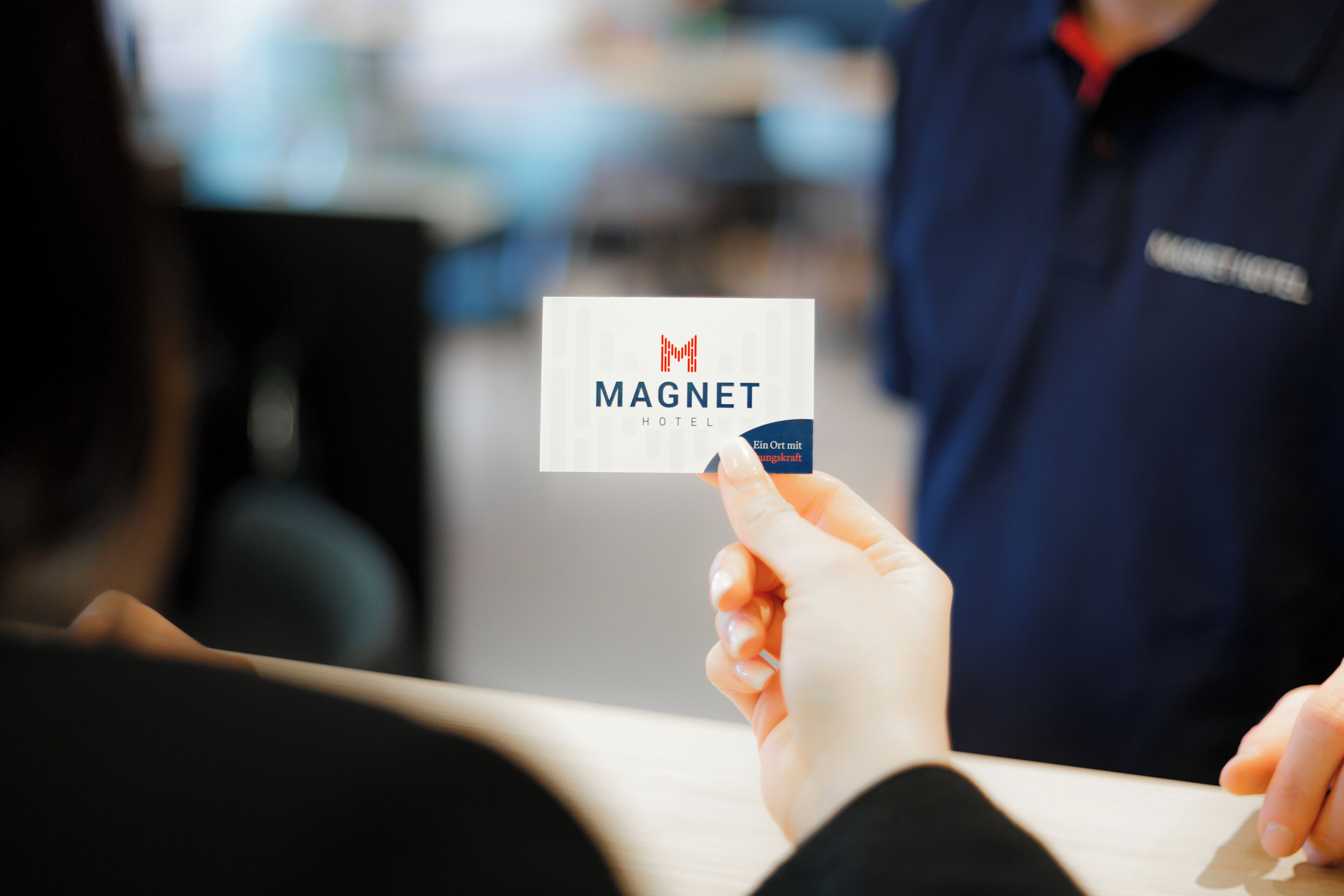 Une main tenant une carte de visite sur laquelle figurent les mots « MAGNET HOTEL » et « Fin Ort mit. »