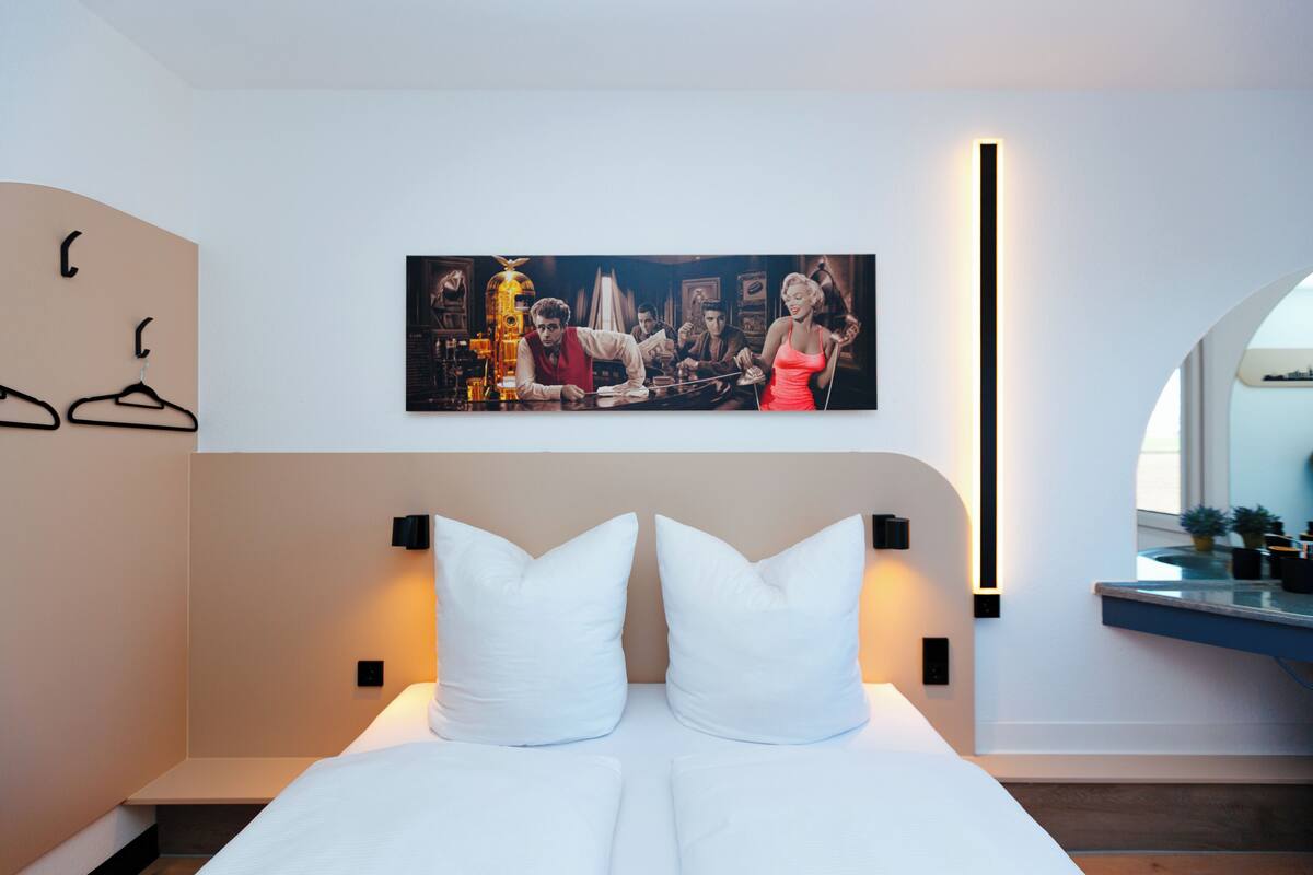 Una habitación de hotel moderna con una cama grande, una obra de arte colgada en la pared y una mesita de noche con lámpara.