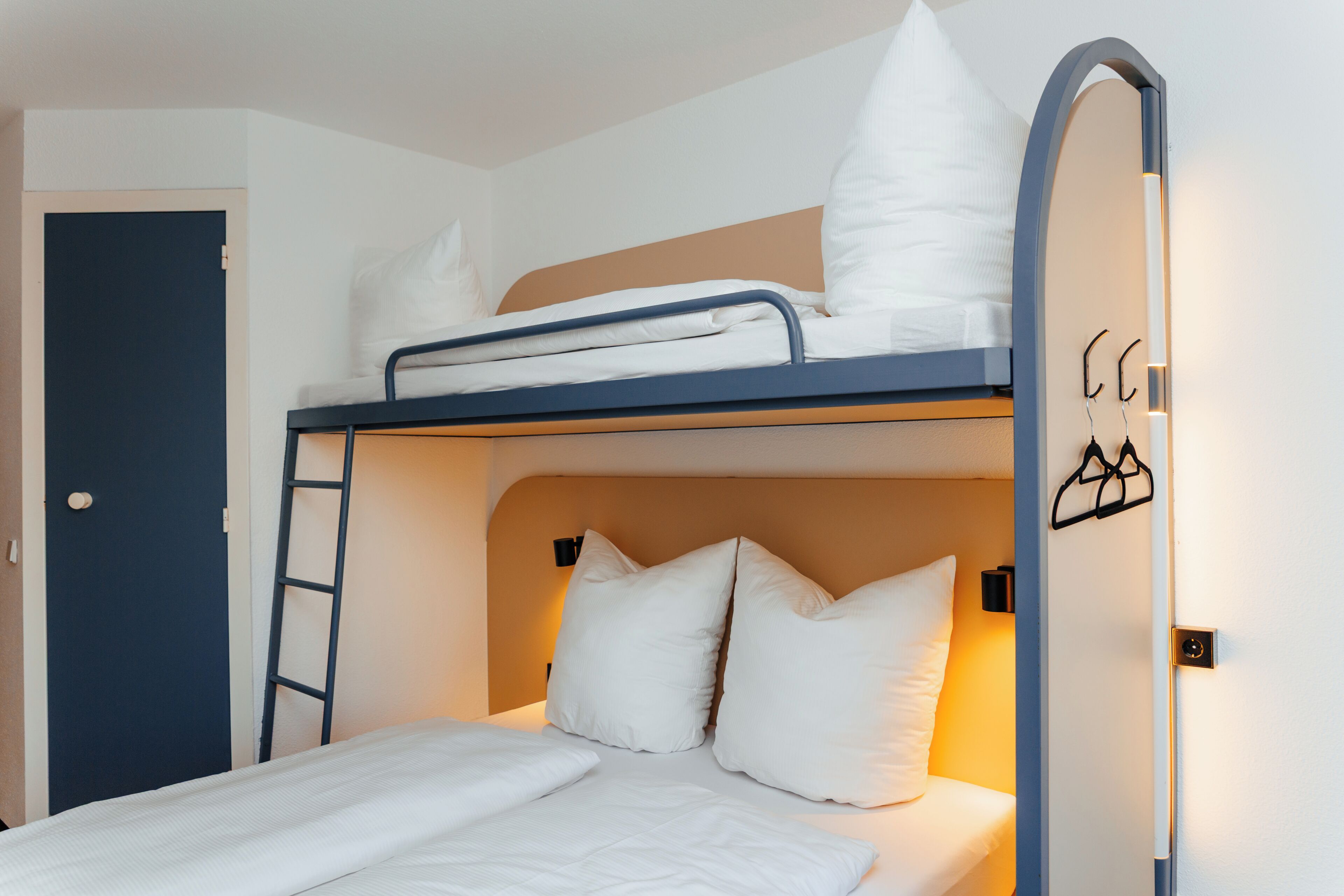 A bunk bed with white bedding, a ladder, and a door with a handle.