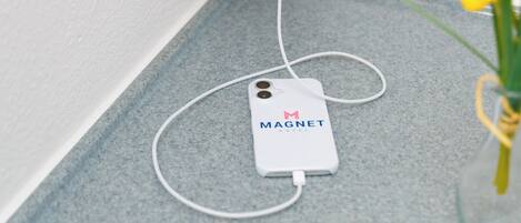 A white device labeled 'MAGNET HOTEL' connected to a wall socket, with a vase of yellow flowers on a blue countertop.