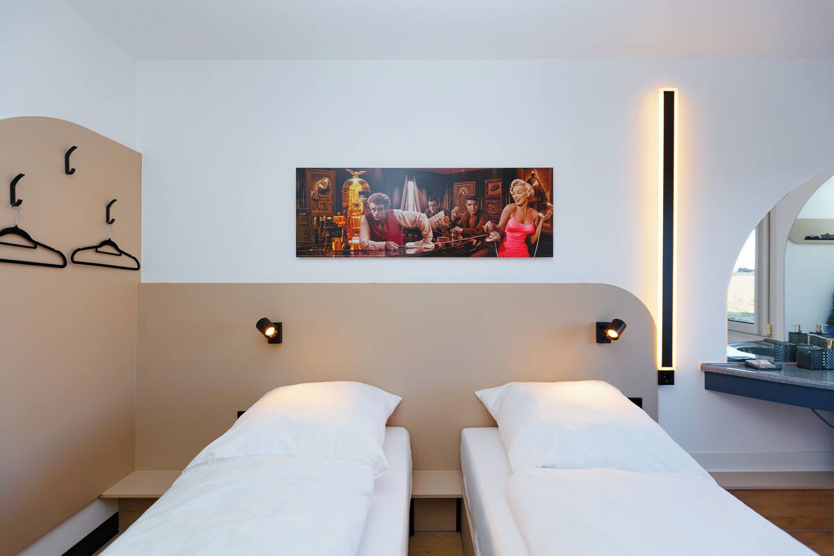 Una habitación de hotel con dos camas, un cuadro en la pared y una mesita de noche con una lámpara.