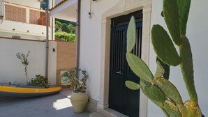 Um pátio com uma porta preta, um cacto, um caiaque amarelo e plantas em vasos.
