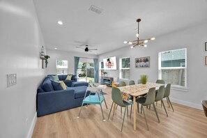 A modern living room with a blue sofa, a dining table with chairs, a ceiling fan, and a fireplace. - Beach Home | Hot tub | Bikes & E-scooters | Game Room (Jacksonville Beach)