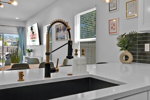 A modern kitchen with a white countertop, a black faucet, and a backsplash. - Beach Home | Hot tub | Bikes & E-scooters | Game Room (Jacksonville Beach)