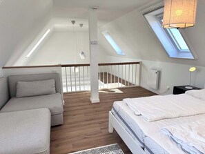 Ein Schlafzimmer mit Dachschräge, einem Bett, einer Couch, einem Nachttisch und einem Oberlicht.
