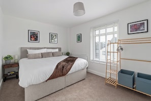 A bedroom with a bed, bedside tables, a radiator, a window with blinds, and a wall-mounted shelf. - Southampton Retreat for 12 Near Waterfront (Southampton)