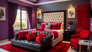 Une chambre à coucher avec un lit, un canapé en cuir, un fauteuil rouge, une table de chevet et un tapis rouge.