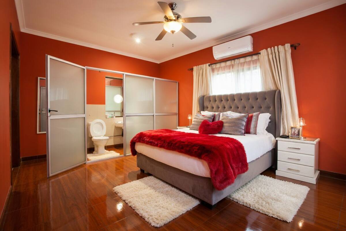 Ein Schlafzimmer mit einem Bett, einem Deckenventilator, einem weißen Nachttisch, einem weißen Teppich, einer weißen Toilette und einem weißen Kleiderschrank.